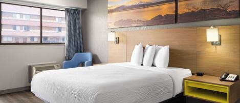 A hotel room with a large bed, a desk with a phone, and a painting of a sunset over a lake.