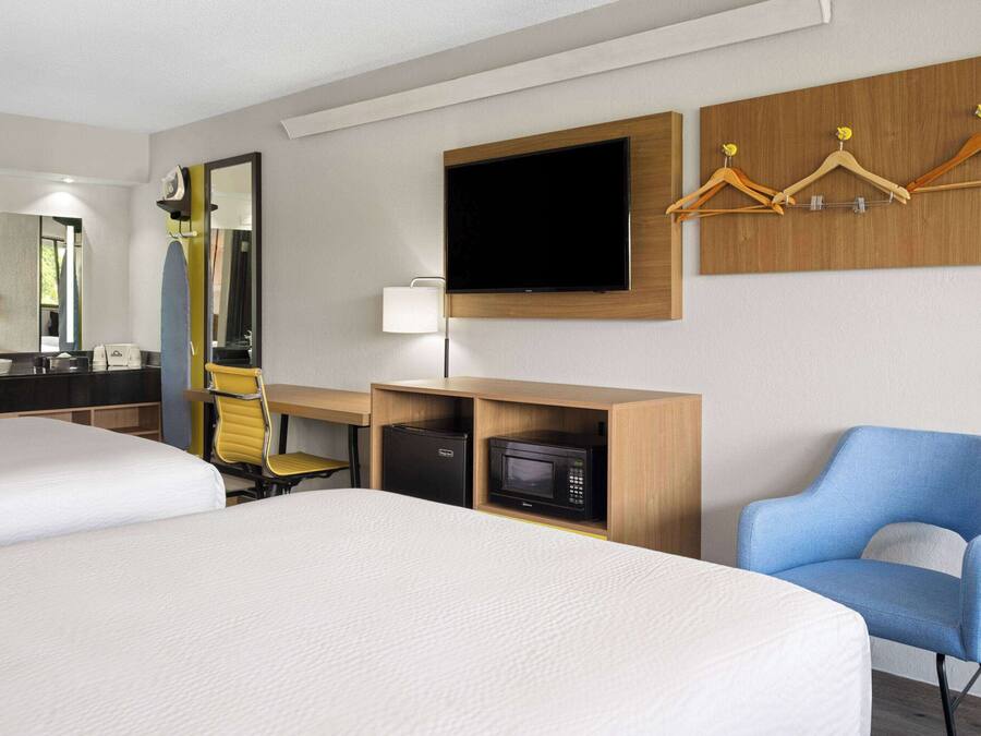 A hotel room with two beds, a desk with a computer, a microwave, a TV, and a chair.