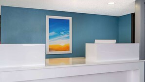 A reception area with a blue wall, a framed painting of a sunset, and a white reception desk. - Days Inn by Wyndham Columbus/Worthington (Columbus)