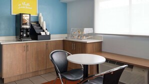 A modern kitchen with a coffee machine, a coffee cup display, and a bench with a table. - Days Inn by Wyndham Columbus/Worthington (Columbus)