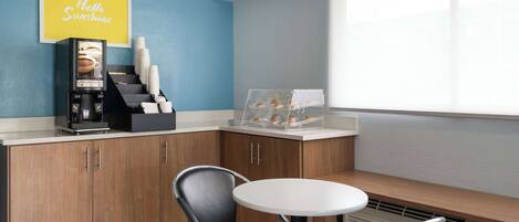 A modern kitchen with a coffee machine, a coffee cup display, and a bench with a table.