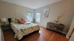 Ein Schlafzimmer mit Bett, Nachttisch, Kommode, Fenstern und Kunstwerken.