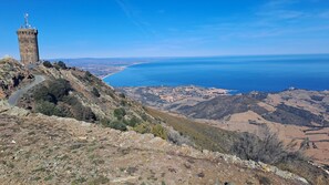 A coastal landscape with a tower, a winding road, and a view of the sea and town below. - Panoramic view with a swimming pool: nestled between the sea and the mountains, in a quiet location. (Laroque-des-Albères)