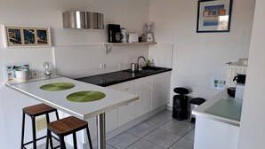 Una cocina moderna con encimera blanca, dos taburetes, campana extractora de acero inoxidable, cafetera y licuadora.
