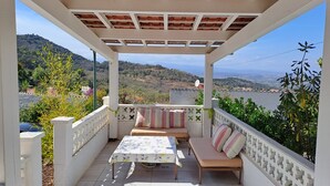 Un espacio de estar al aire libre cubierto con una mesa y sillas, con vistas a un paisaje pintoresco con colinas y una masa de agua.