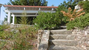 Una escalera de piedra que sube hacia una pérgola blanca con tejado de tejas rojas.