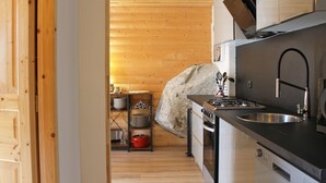 Cuina compacta amb parets de fusta, fogó de gas, rentapelats i un petit taulell.