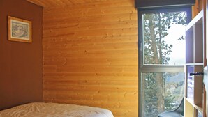 Habitació amb parets de fusta, un llit, una finestra amb vista a arbres i una cadira.