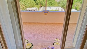 Ein Balkon mit Blick auf das Meer und die Berge, ein Verbotsschild mit der Aufschrift 'Nichtklettern', ein Tisch mit Blumen und einer Karaffe.