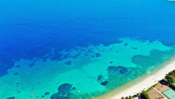Eine Vogelperspektive einer Küstenlandschaft mit klarem, blauem Wasser, einem Sandstrand und einer kleinen Insel mit Vegetation.