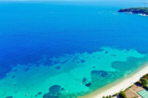 An aerial view of a coastal area with clear blue waters, a sandy beach, and a small island with vegetation.