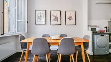 Een eetruimte met een houten tafel en grijze stoelen, een raam met gordijnen en drie ingelijste foto's aan de muur.
