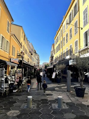A pedestrian street with yellow buildings, outdoor seating, and potted plants.