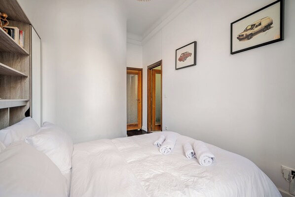 Una habitación de hotel con una cama, un estante de madera con libros y dos cuadros en la pared.