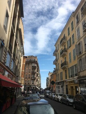 A street view with multi-story buildings, parked cars, and pedestrians.