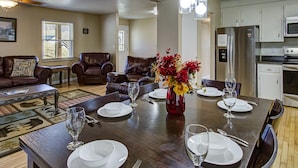Un coin repas avec une table en bois dressée pour quatre personnes, entourée de chaises en cuir. Un vase rempli de fleurs rouges est posé sur la table.