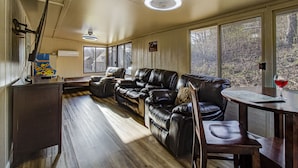 Un salon chaleureux avec un canapé en cuir, une table à manger en bois et de grandes fenêtres donnant sur l’extérieur.