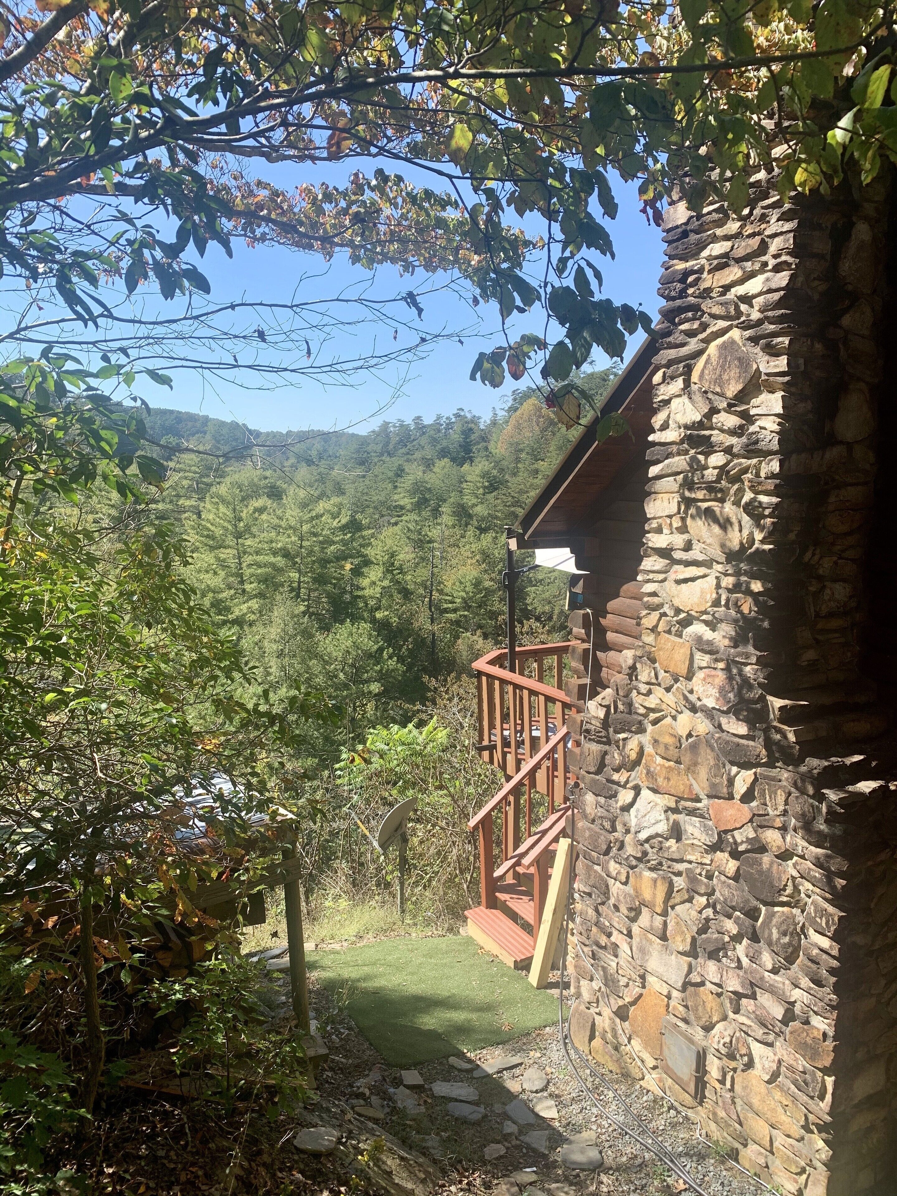 A stone building with a wooden deck and a view of a forested valley.