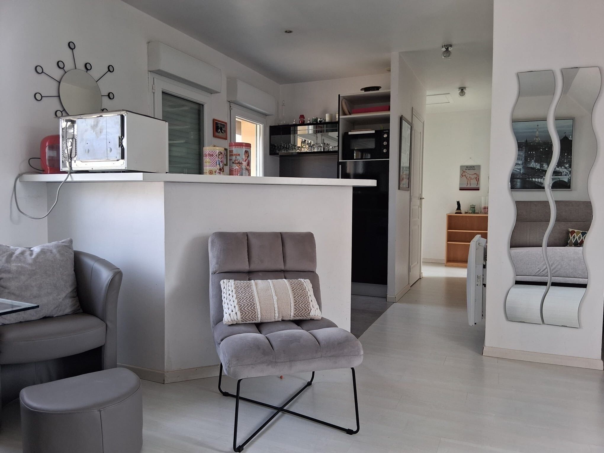 A modern kitchen with a built-in island, grey upholstered chairs, and a dining area with a grey sofa and ottoman.