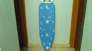 A blue ironing board with a star and moon pattern in a hallway with wooden doors and tiled flooring. - Home away from home (Nyeri)