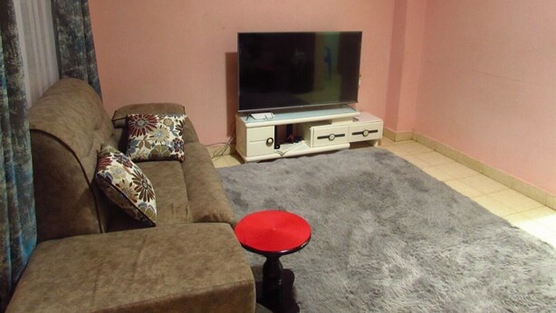 A living room with a sofa, a red stool, a television on a stand, and a framed picture on the wall. - Home away from home (Nyeri)