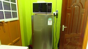 A kitchen with a stainless steel refrigerator, a microwave on top, and a wooden door. - Home away from home (Nyeri)