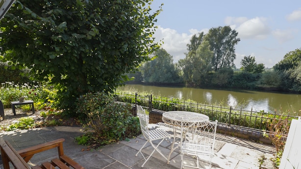 Une terrasse avec un banc en bois et une table et des chaises en métal, donnant sur une rivière.