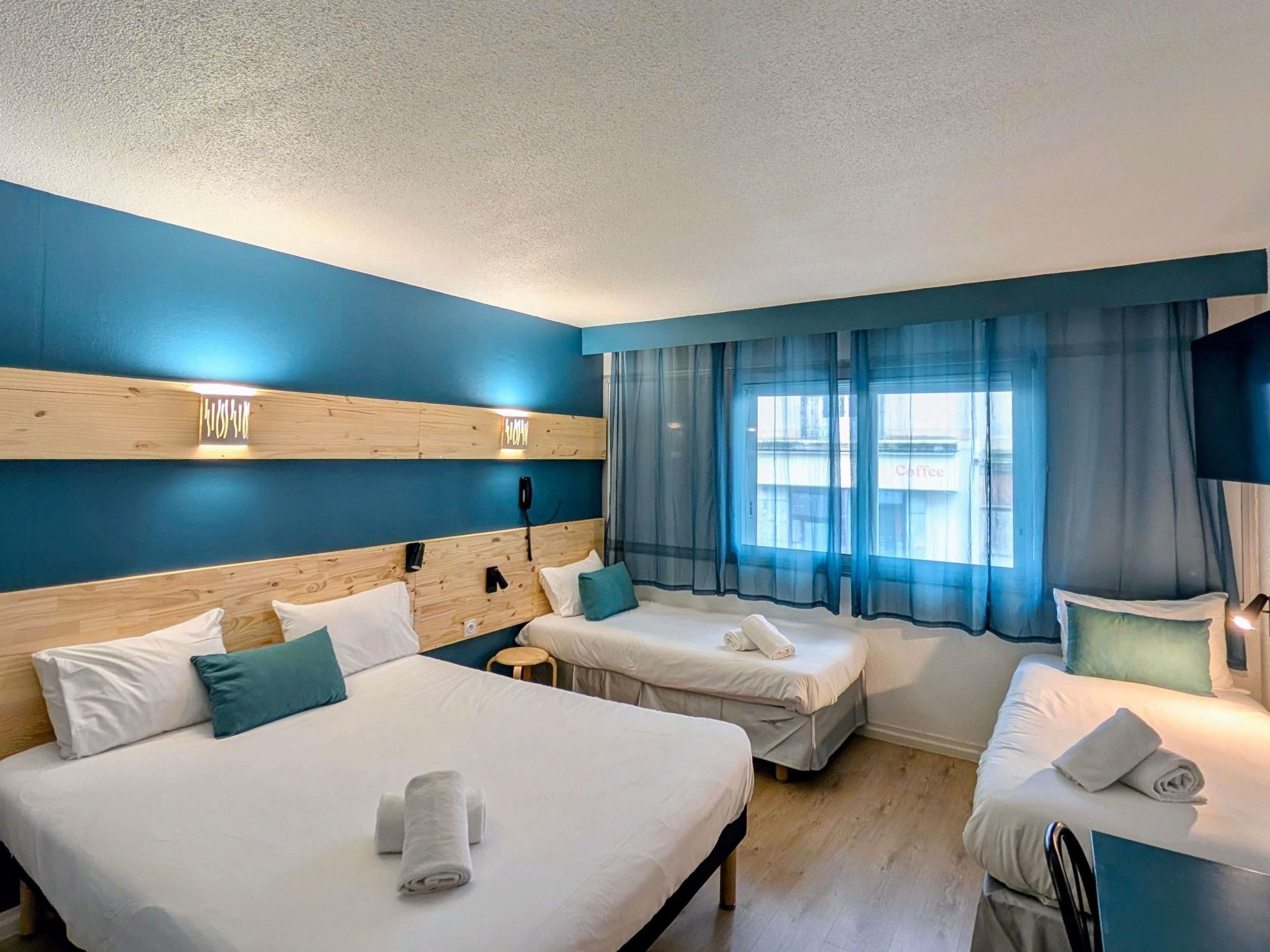 A hotel room with two beds, a wooden headboard, a phone, and a window with blue curtains.