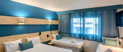 A hotel room with two beds, a wooden headboard, a phone, and a window with blue curtains.