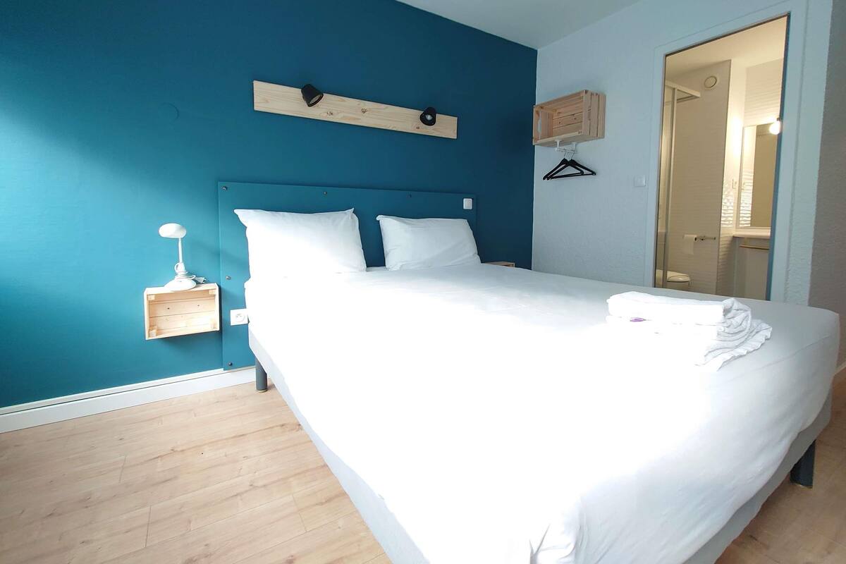 Une chambre à coucher avec un grand lit, une table de chevet avec une lampe, une tête de lit en bois, un miroir et une petite étagère en bois.