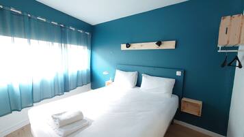 A neatly made bed with white linens and towels, a bedside table with a lamp, and a wooden headboard.