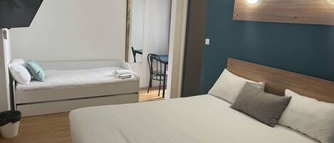 A hotel room with a large bed, a smaller sofa, a desk, and a chair.