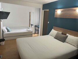 Hotellihuone, jossa on suuri sänky, pienempi sohva, työpöytä ja tuoli.