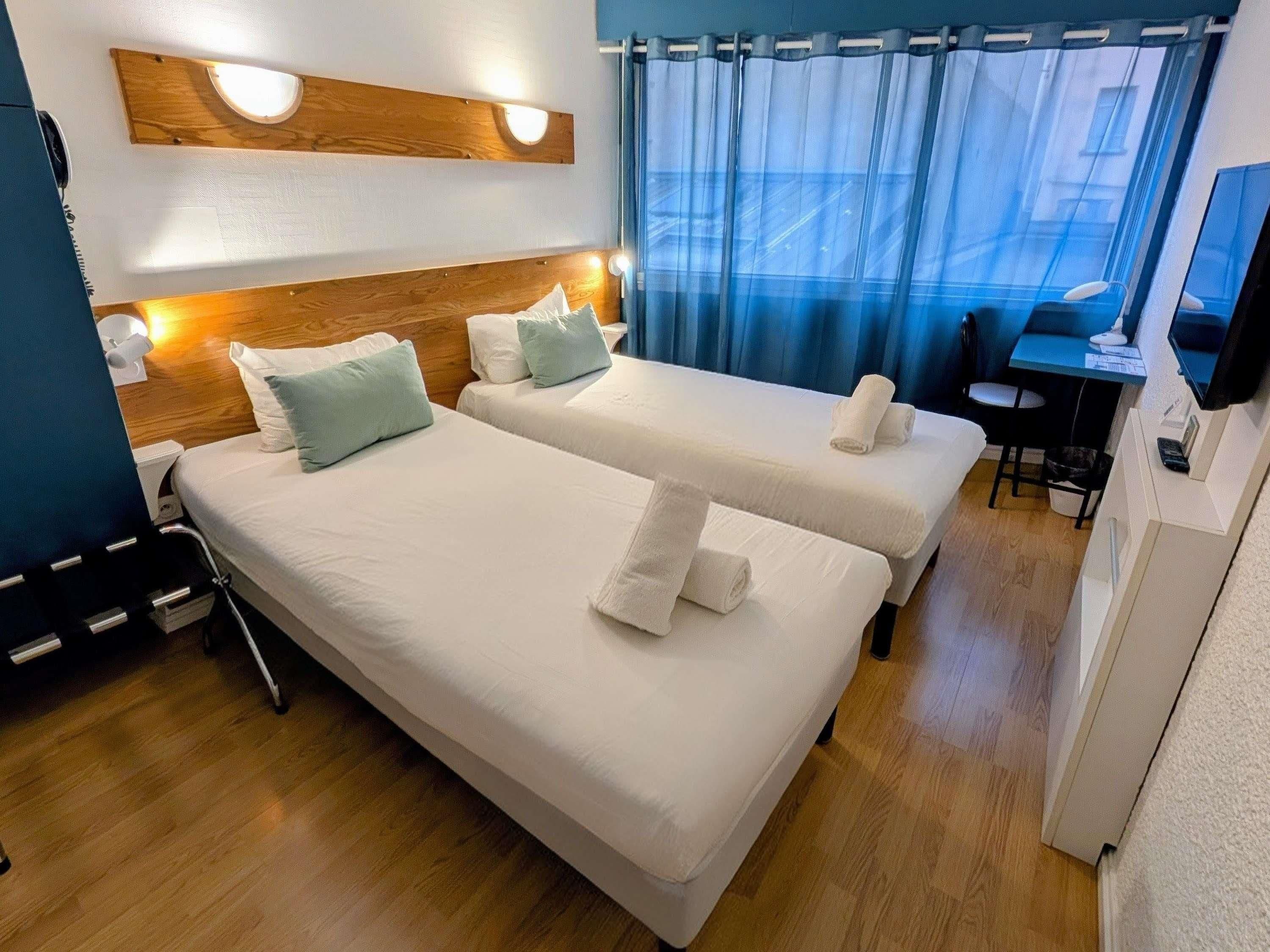 Une chambre d’hôtel avec deux lits, un bureau, une chaise et un téléviseur.