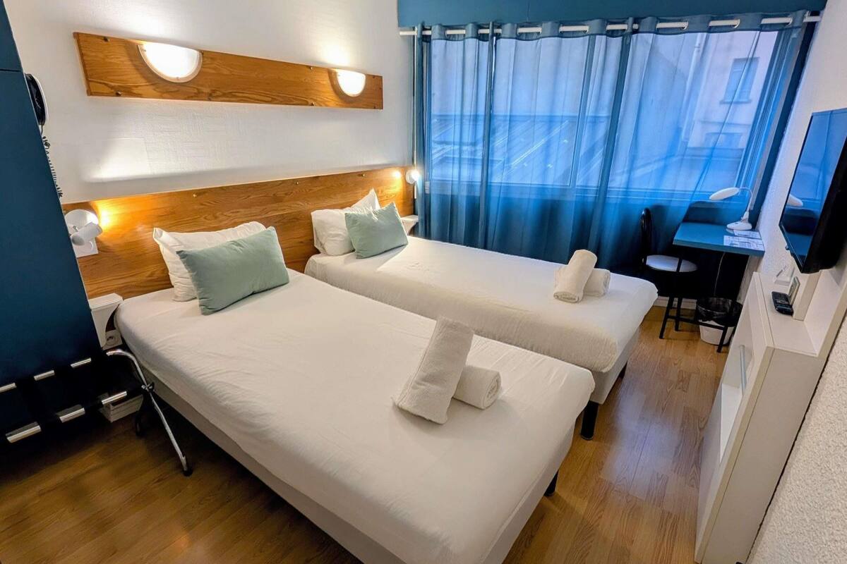 A hotel room with two beds, a desk, a chair, and a TV.