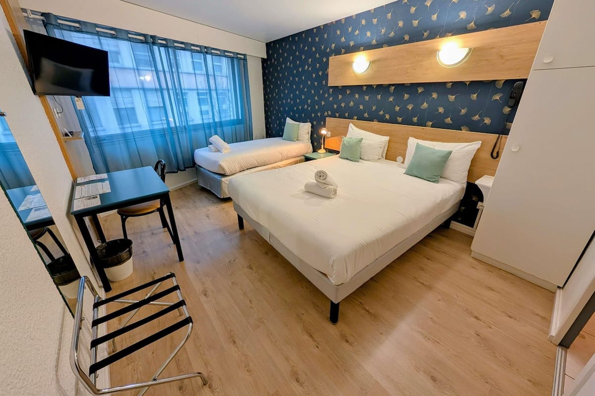 Une chambre d’hôtel avec un lit, un bureau, une chaise, une télévision et une fenêtre avec des rideaux.
