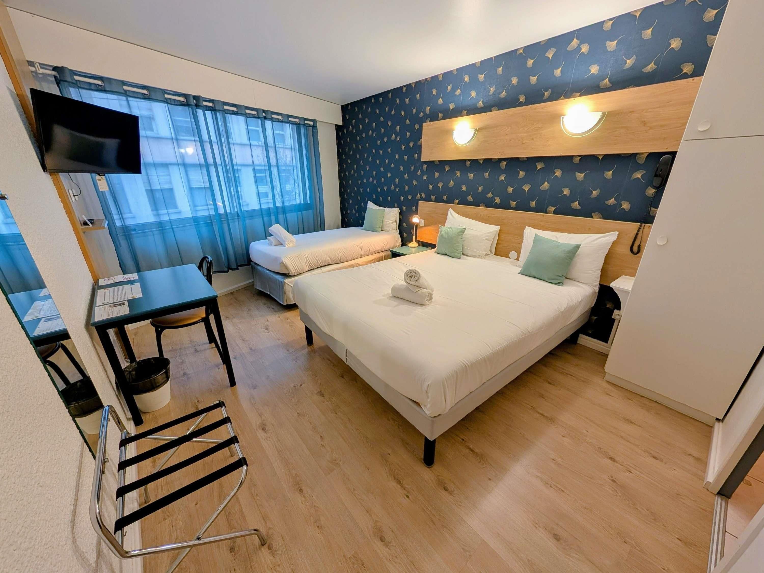 A hotel room with a bed, a desk, a chair, a TV, and a window with curtains.
