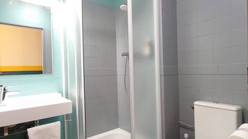 A modern bathroom with a glass-enclosed shower, a white toilet, and a sink with a mirror above it.