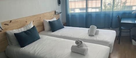 Habitación de hotel con dos camas, cabecero de madera, un escritorio y una silla.
