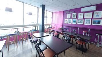A restaurant interior with tables and chairs, large windows, and a purple wall with framed pictures.