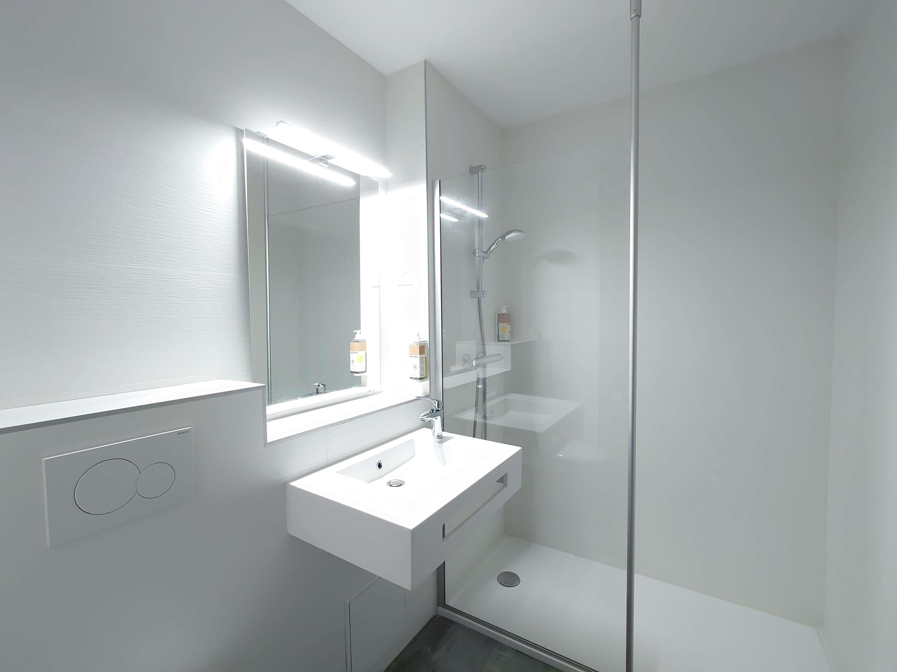 Une salle de bain moderne avec un lavabo blanc, un miroir et une douche à parois de verre.