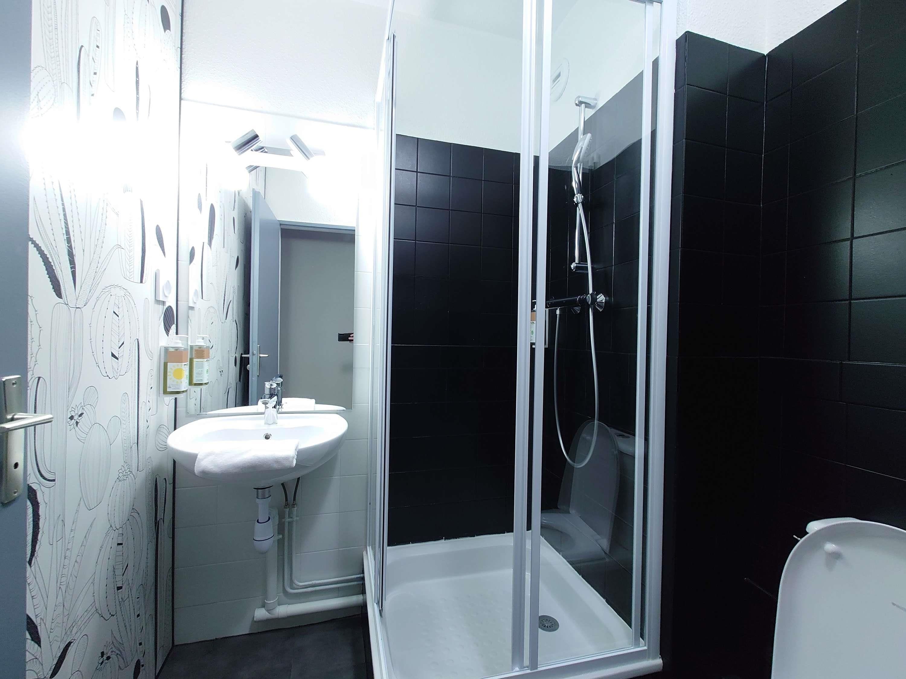 A modern bathroom with a glass shower enclosure, a white sink, and black tiled walls.