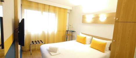 A hotel room with a bed, a desk, a chair, and a TV.