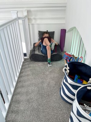 A child lying on a bed with a pillow, a striped bag with toys, and a white railing.