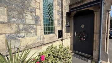 A stone building with a black door, a window with a grid pattern, and a sign that reads 'The Old Chapel'.