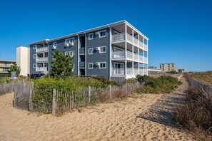 Un edificio de varios pisos con balcones, cerca de una playa arenosa con una valla de madera.