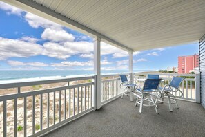 A covered outdoor area with a view of the beach, featuring a white railing, a table with chairs, and a clear sky. - Direct Oceanfront Top Floor | Large Balcony + Stunning Views (Ocean City)