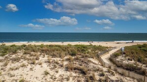 En strand med ett trästaket, sanddyner och havet.