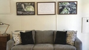 Un canapé gris agrémenté de coussins à motifs, une petite table d’appoint en bois et une citation encadrée accrochée au mur.