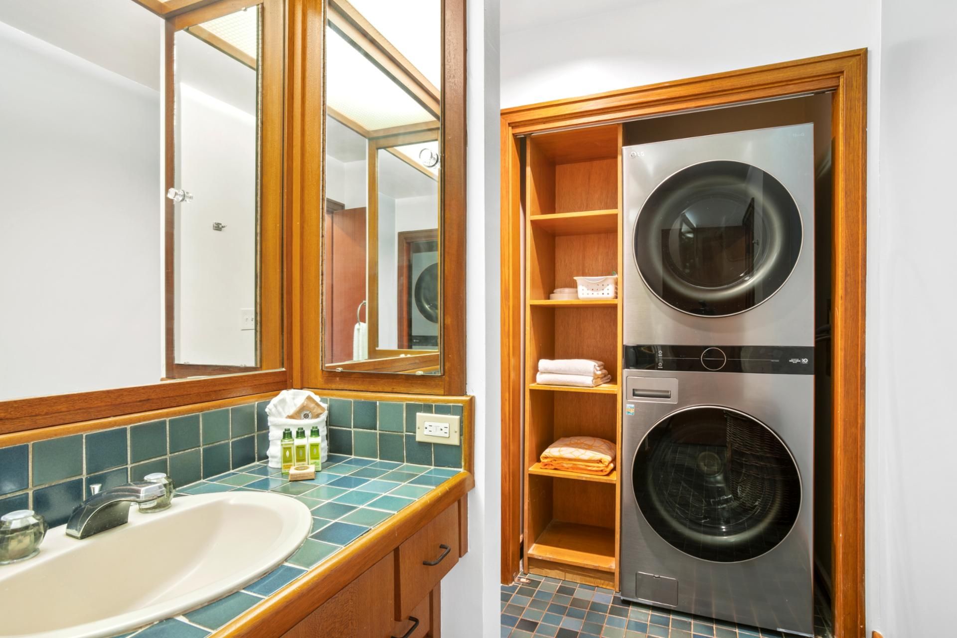 A bathroom with a sink, mirror, and wooden shelving unit containing a washing machine and dryer.